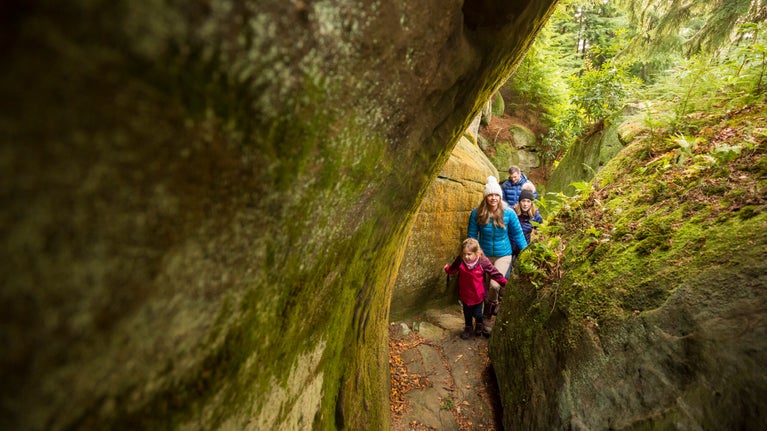 A family following a rugged trails between the high-sided rocks at Cragside, Northumberland.